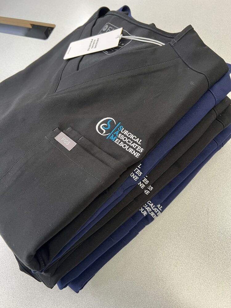 A folded stack of navy and black medical scrubs with an embroidered left-chest logo.