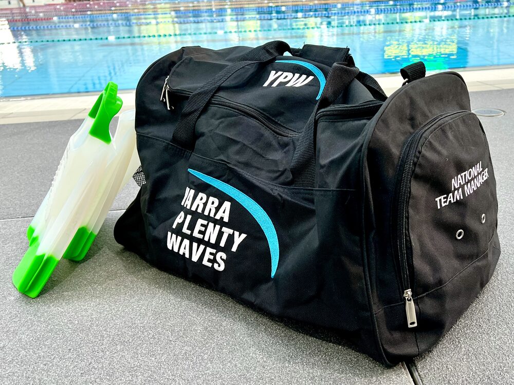 An embroidered black team kit bag beside a swimming pool.